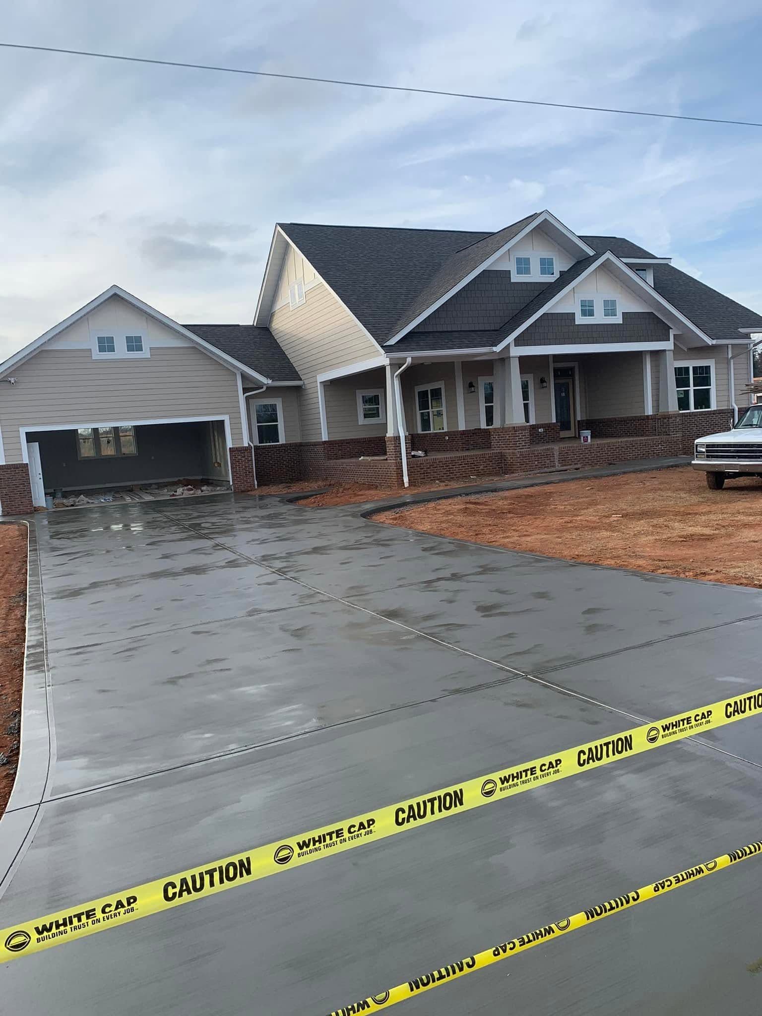 Newly constructed house with a wet concrete driveway cordoned off by yellow caution tape.
