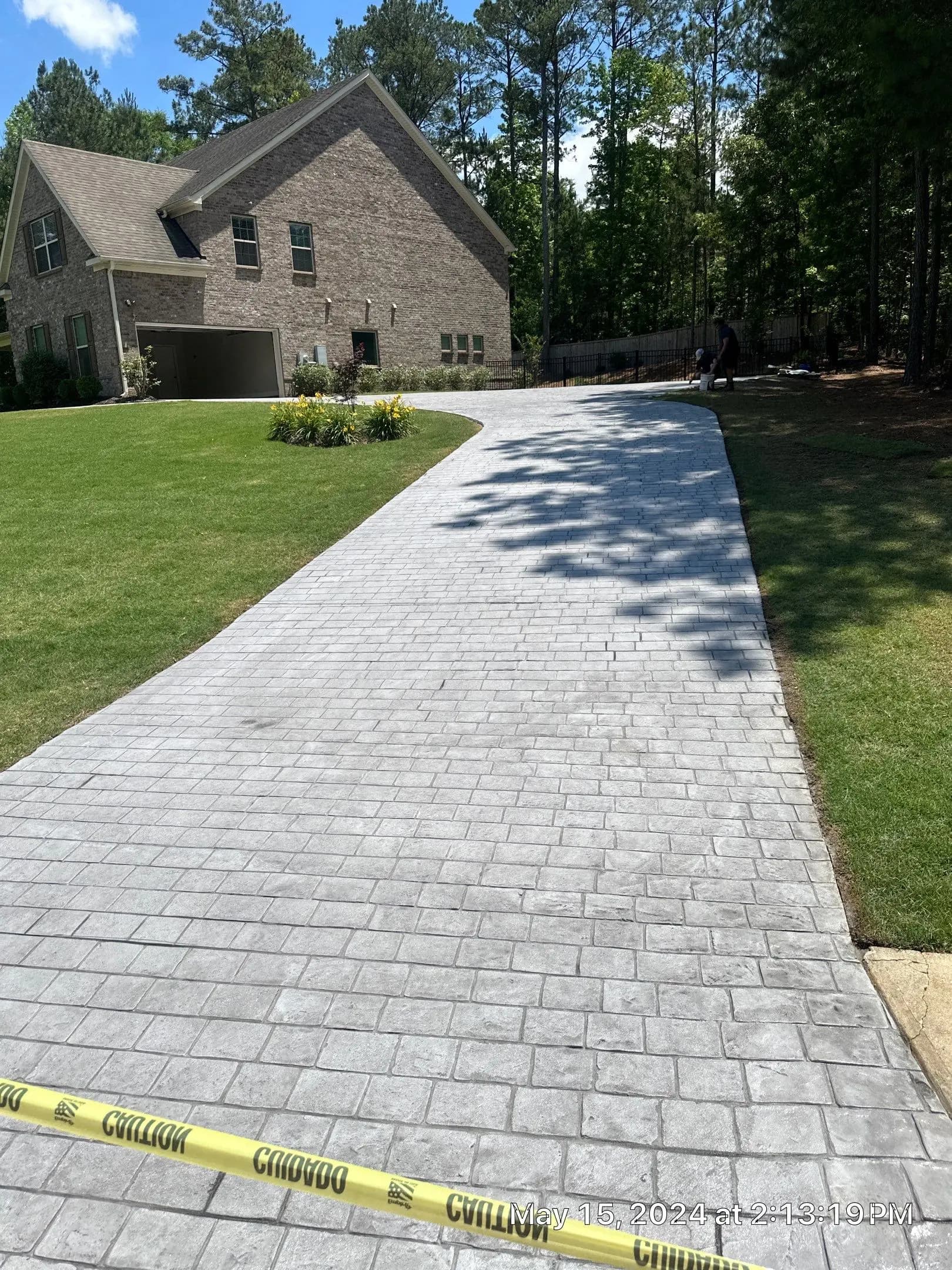 Gray stamped concrete driveway with a cobblestone pattern leading to a large brick house.
