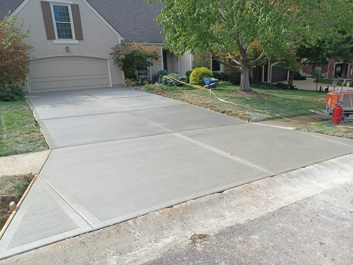 Freshly poured concrete driveway with clean expansion joints in front of a suburban house.
