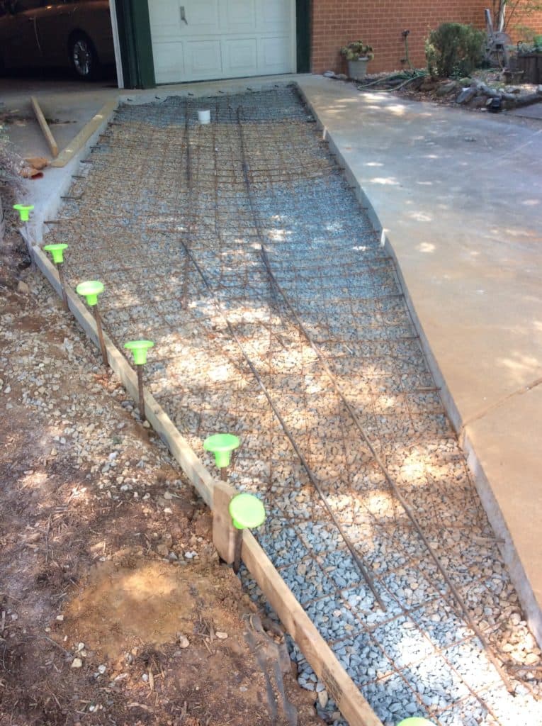 Wire mesh over gravel base for a concrete path with wooden forms and green caps.