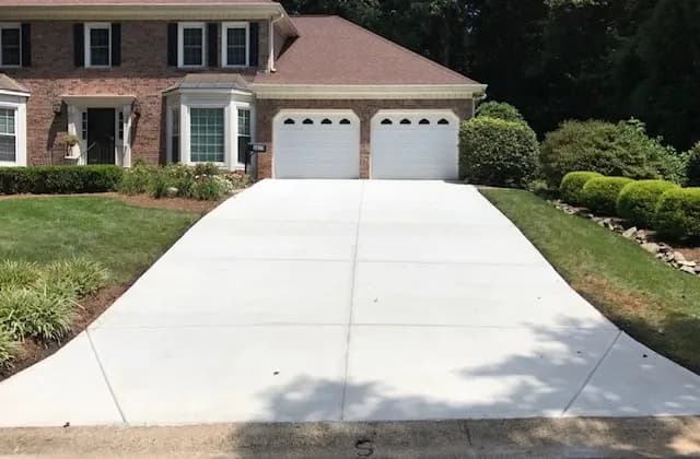 Pristine white concrete driveway leading to a two-car garage of a suburban brick house.